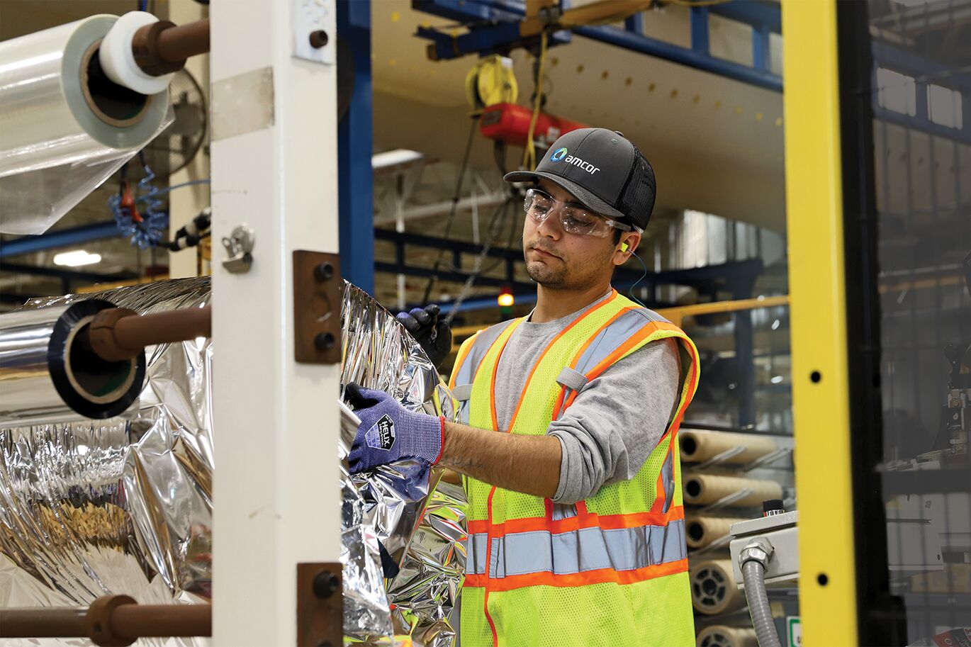 Mashoqullah Haseen, roll wrapper at Amcor, takes rolls of produced film and applies a protective wrap prior to palletizing, using lifting equipment to maintain safety and protect him from injury.