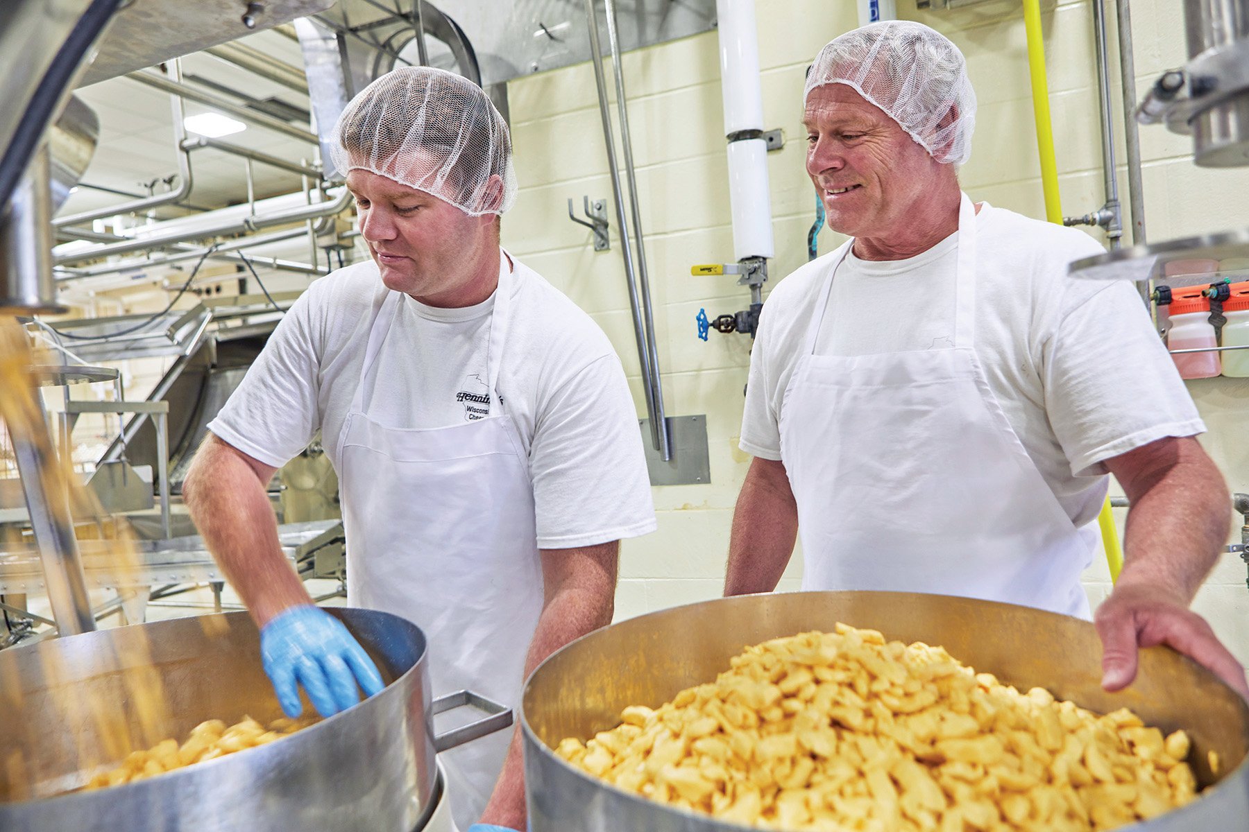 Certified Master Cheese Maker Kerry Henning (right) and fourth‑generation licensed cheesemaker Zachary Henning (left) fill hoops, the containers used to mold curds.