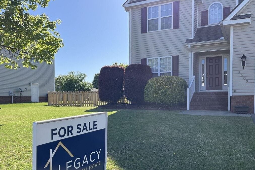 A Legacy Real Estate sign stands in the yard of a house listed for sale.